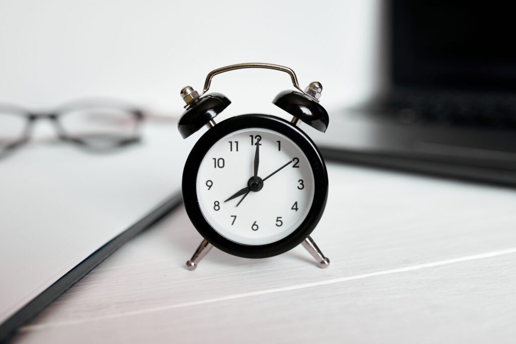 Time management concept, office workplace, notebook, computer, laptop and black alarm clock on white wooden office desk, copy space.